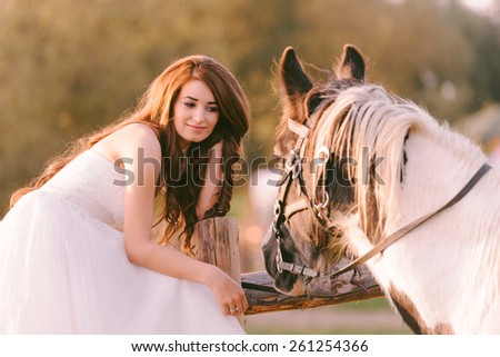 Beautiful and stunning bride, looking at her horse in the nature, on her wedding day
