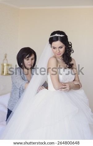 Beautiful, stunning bride, getting dressed in her wedding day by her mother