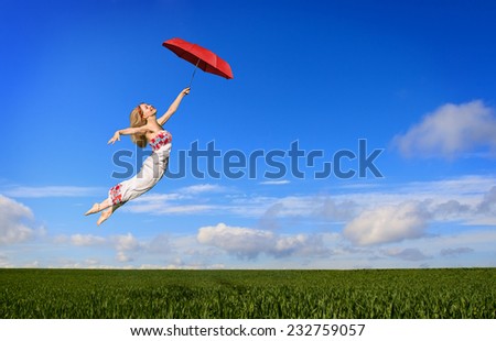 Beautiful young woman flying on a green meadow with a red umbrella