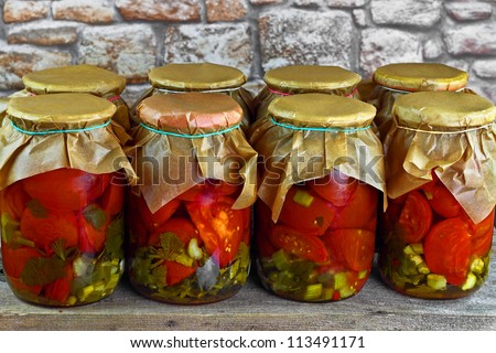 Jars with pickled red tomatoes on wooden shelf against stone wall