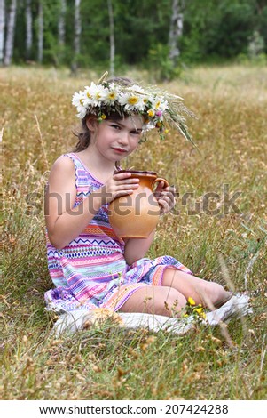 Little girl sitting on grass with jug in hands. Her lips smeared in milk