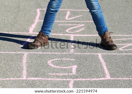 Human legs in jeans and boots stand on asphalt lined to play hopscotch with shadow outdoor in sunny day