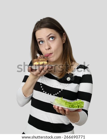 Diet, nutrition, weight loss and choice concept - Young woman makes choose between cake and lettuce on gray background