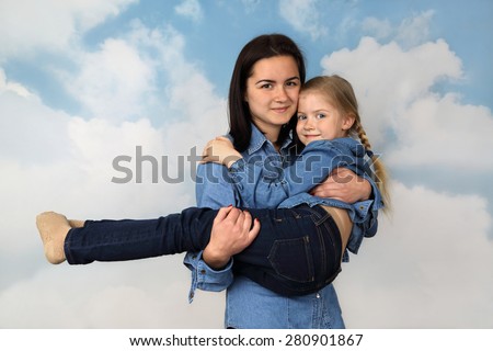 Older girl carries younger sister on hands on cloudy blue sky background - Family feelings and love concept