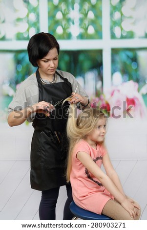 Brunette woman hairdresser cuts little blonde girl long hair