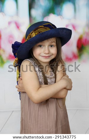 Cute little girl in too big hat smiles cringed with crossed arms