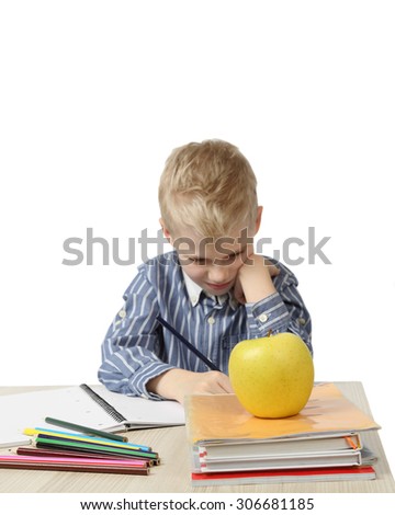 Schoolboy sits near the desk with school supplies and big apple on foreground isolated on white background with focus on apple - learning and homework