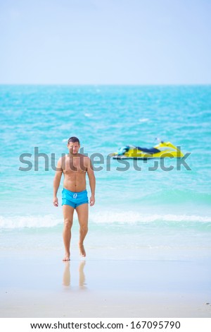 handsome man walking out of the water after jet-sking on the beach at summer holiday