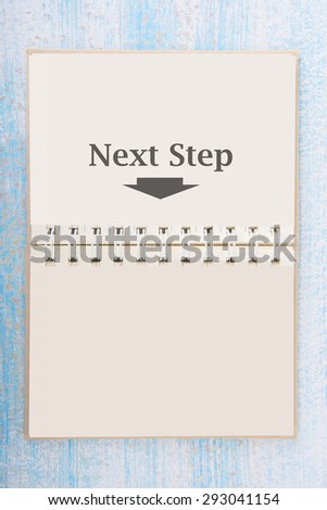 Notebook with next step on blue wooden desk