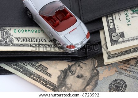 Miniature car over a leather wallet with dollars