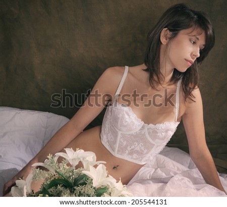 Beautiful Woman in White Vintage Lingerie With White Flowers on White Comforter