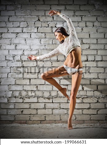 Young dancing woman on grey brick wall background (normal version)