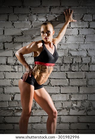 Muscular woman on grey brick wall (normal version)