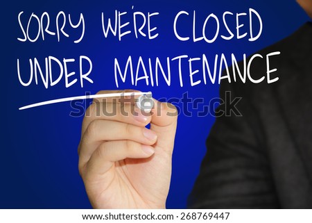 Internet concept image of a hand holding marker and write Sorry We are Closed Under Maintenance over blue background