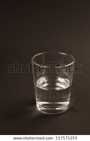 Half full or half empty glass of water. Black background.