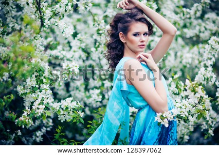 outdoor portrait of a beautiful brunette woman in blue dress among blossom apple trees