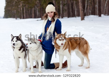 Happy young woman playing with siberian husky dogs in winter forest