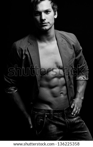 Black and white portrait of sexy man with open jacket over dark background. Vertical image