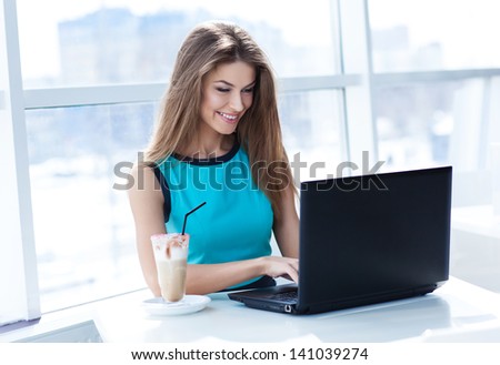 Portrait of beautiful smiling woman sitting in a cafe with black laptop