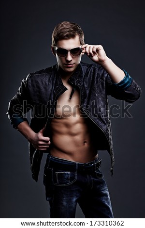 Young handsome macho man in sunglasses with open leather jacket revealing muscular chest and torso