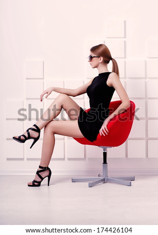 Sexy woman in short black dress and sunglasses sitting on a chair. Fashion shot