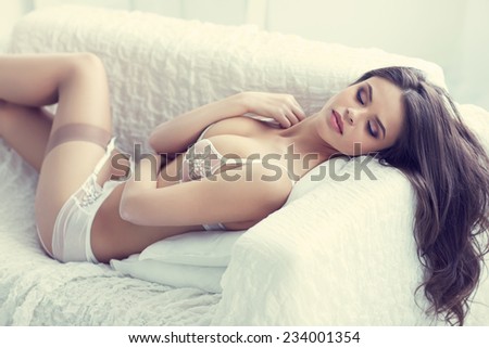 close up portrait of beautiful alluring young woman in white sexy lingerie lying in sofa