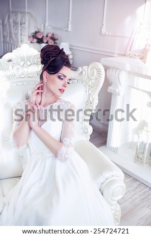 Young gorgeous bride is sitting in antique armchair. Soft light and colours