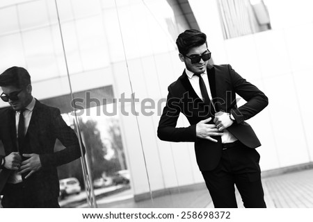 handsome stylish man in elegant black suit and sunglasses in the street. Black and white image