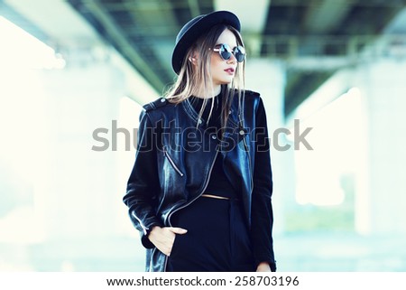 fashion model in sunglasses, hat and black leather jacket posing outdoor.