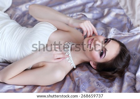 Closeup portrait of beautiful bride lying in the bed. Wedding dress, makeup, hair