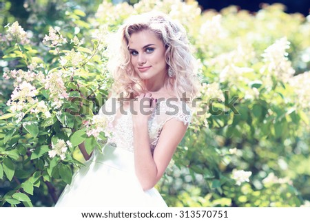 Beautiful bride posing outdoor. Wedding dress, curly blond hair.