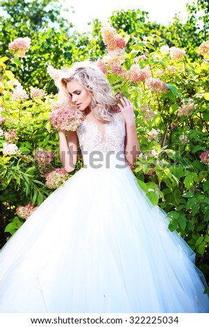 Beautiful bride posing outdoor among the flowers. Wedding dress, curly blond hair.