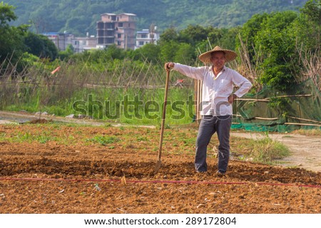 YANGSHUO, CHINA - MAY 01, 2015: A Chinese farmer is working on fields next to Yulong river in Yangshuo. Agriculture is a vital industry in China, employing over 300 million farmers.