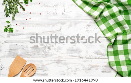 White wooden table covered with green tablecloth and cooking utensils. View from top. Empty tablecloth for product montage. Free space for your text