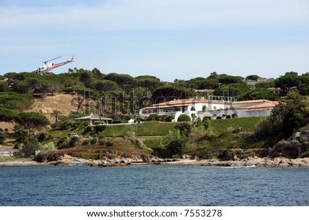 Helicopter is flying away from a luxury residence among old trees on a coast of Saint Tropez, French riviera