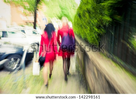 Two  unrecognizable women in red going ahead, intentional motion blur