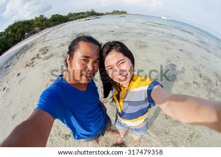 asian people take a photo in selfie style on the beach in mist curved fish-eye lens.