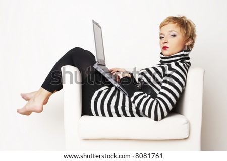 Nice blond girl sitting on the white chair in black and white dress and working laptop