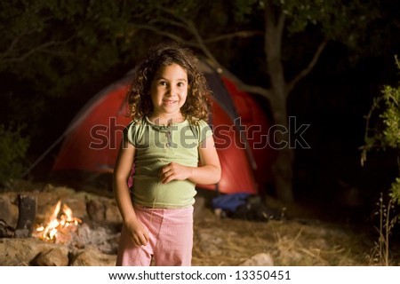 little girl at a camp at night in front of a red tent and a campfire
