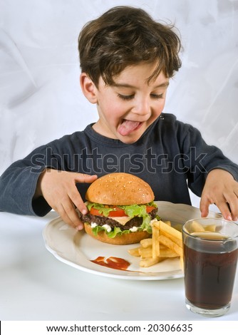 young boy eating cheeseburger with french fries and coke