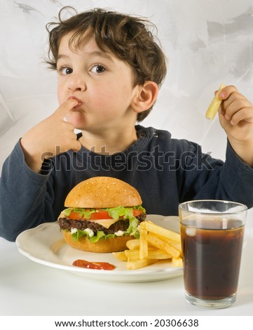 young boy eating cheeseburger with french fries and coke