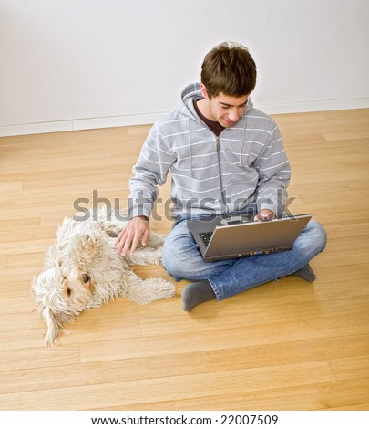 teenager with a laptop computer and his dog on a parquet floor