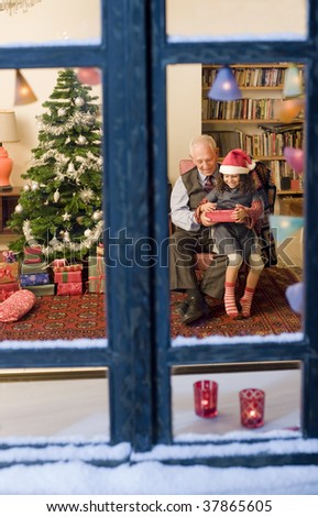 grandfather giving Christmas present to his little granddaughter watched from a snowy window