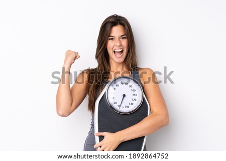 Teenager Brazilian girl holding a scale over isolated white background with weighing machine and doing victory gesture Photo stock © 