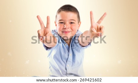 Boy making a victory sign on wooden chair over ocher background