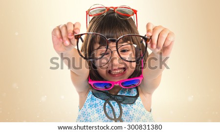 Girl wearing many sunglasses over ocher background