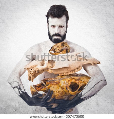 prehistoric man holding animal skulls over grey background