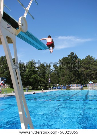 Boy jumping off the high diving board at a public swimming pool.