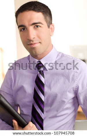 A good looking business executive looking at the camera with a serious look on his face holding a leather pad wearing a purple shirt and tie