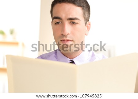 A cute guy with a serious expression looking at the contents of a manila folder. Man is in focus and the folder is out of focus.
